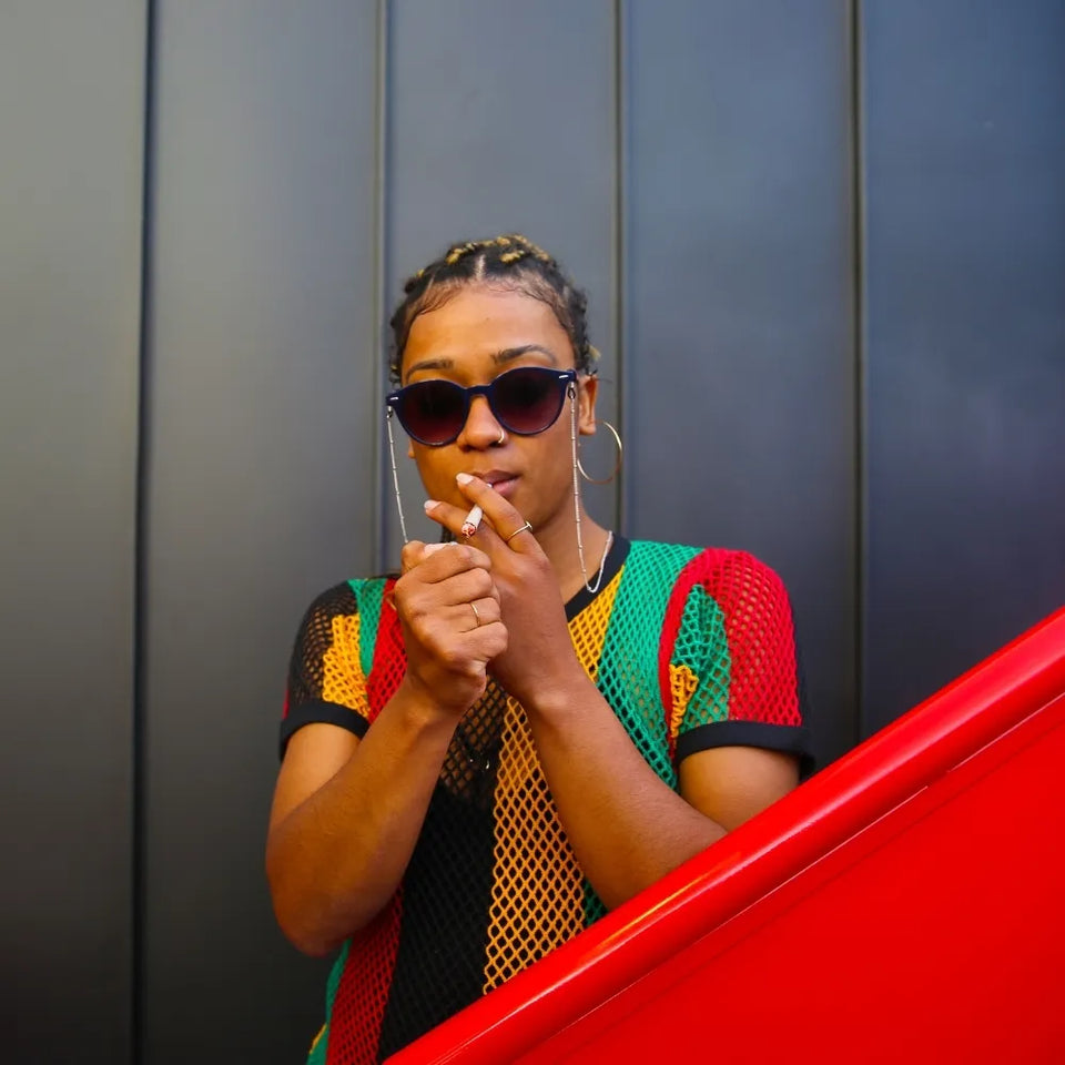 Jeune femme en tenue rasta allumant un joint de CBD â GR33NZ