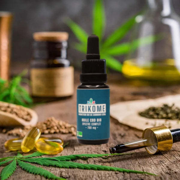 Flacon dâhuile CBD bio gr33nz en gros plan, accompagnĂ© dâune pipette, de capsules dâhuile, de graines et de feuilles de chanvre sur un fond naturel.