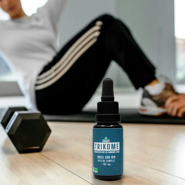 Huile de CBD bio pour la récupération aprÚs le sport, avec haltÚre en arriÚre-plan.