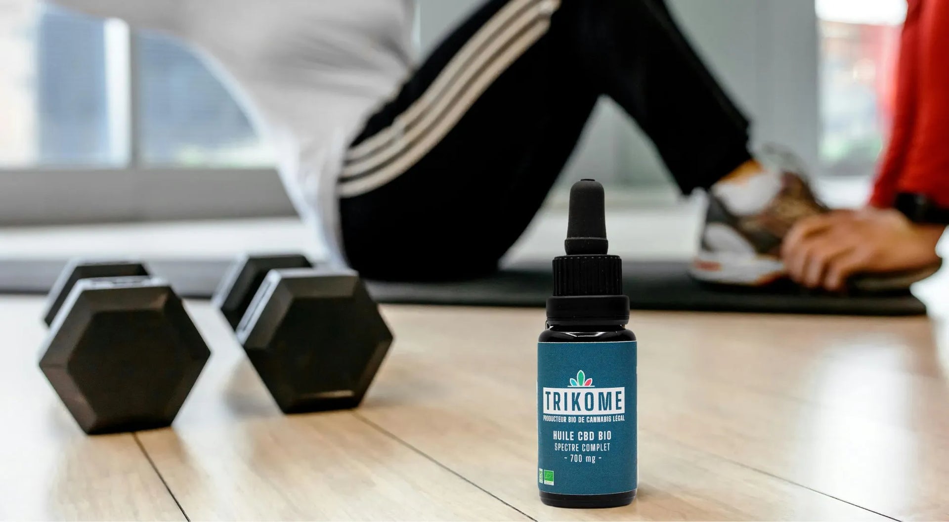 Flacon d’huile de CBD bio gr33nz au premier plan, avec une personne faisant du sport en arrière-plan