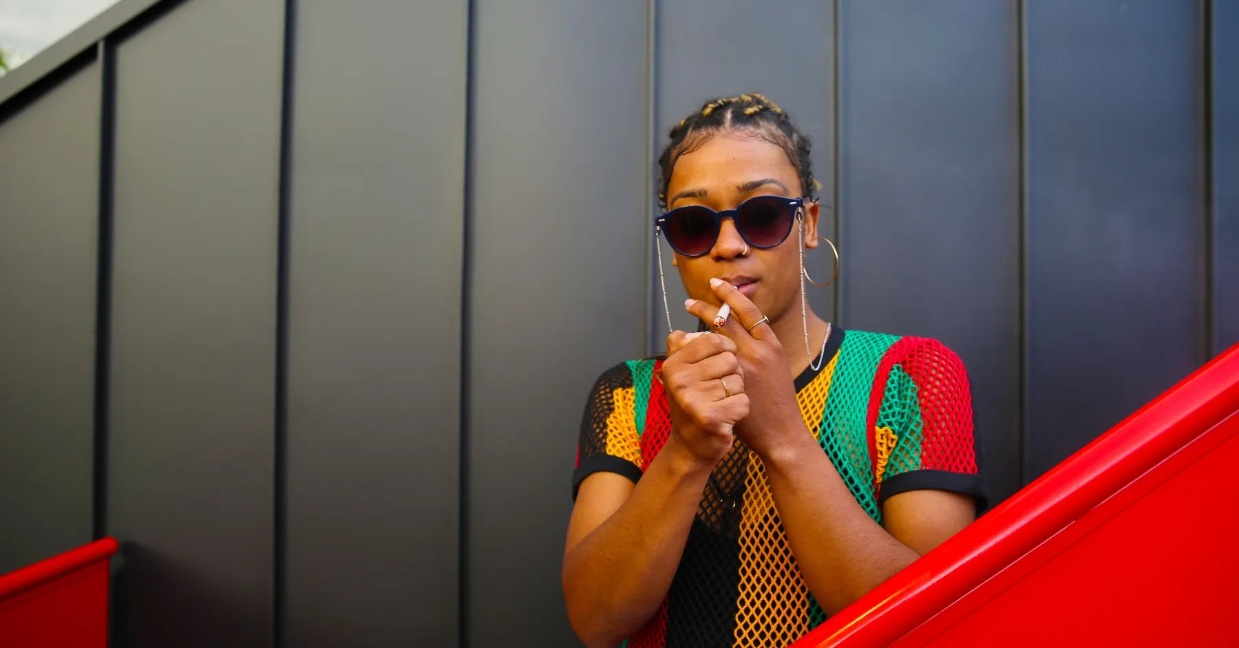 Jeune femme en tenue rasta allumant un joint de CBD – GR33NZ