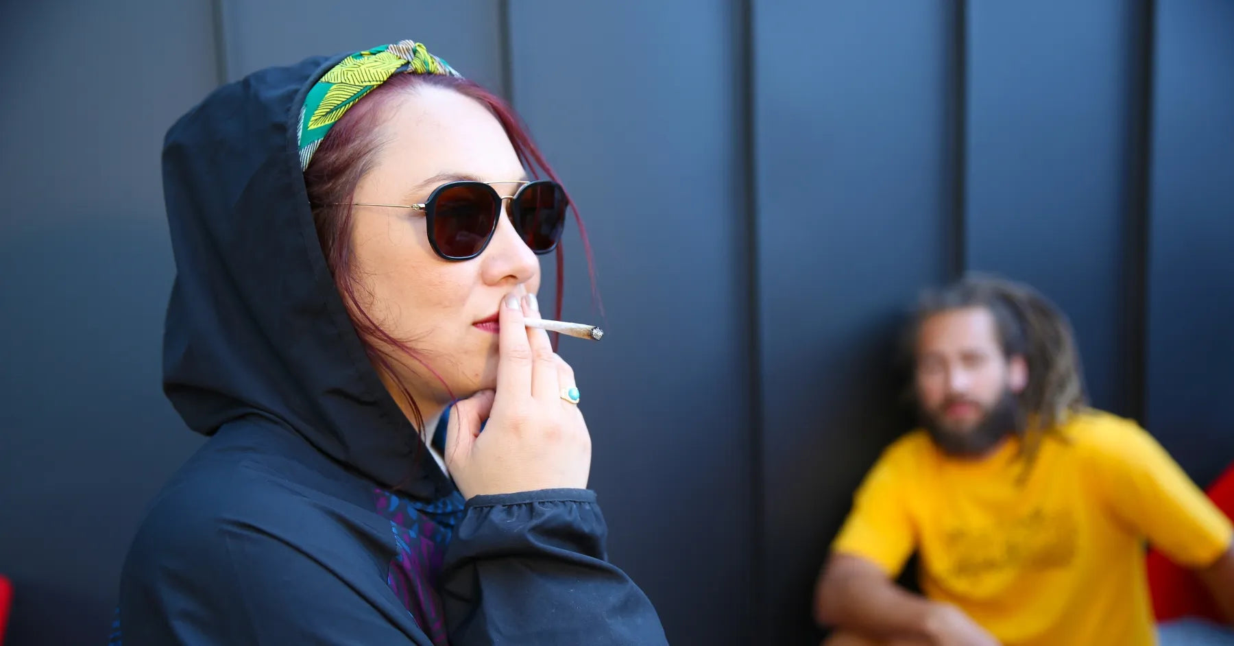 Femme décontractée fumant un joint de CBD, avec un homme en arrière-plan – GR33NZ