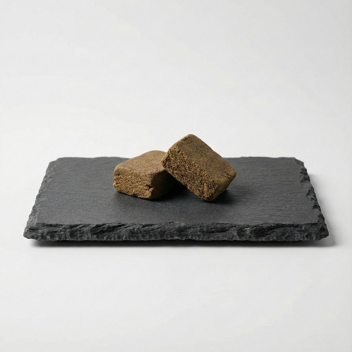 Velvet Hash GR33NZ présenté sur ardoise : résine CBD bio pure, issue de pollen pressé à froid. Texture dense, couleur dorée et taux de THC inférieur à 0,3 %.