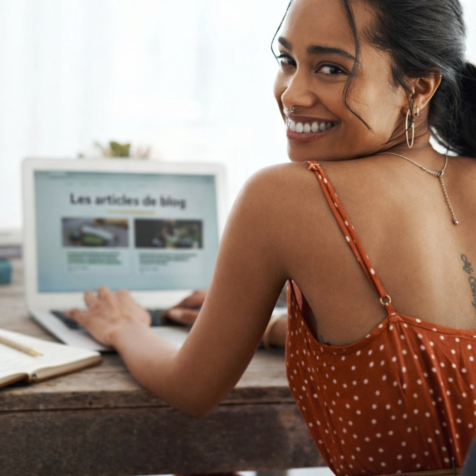 Portrait d'une jeune femme souriante travaillant sur son ordinateur portable, illustrant la consultation d'articles de blog et de conseils bien-être sur le site GR33NZ.