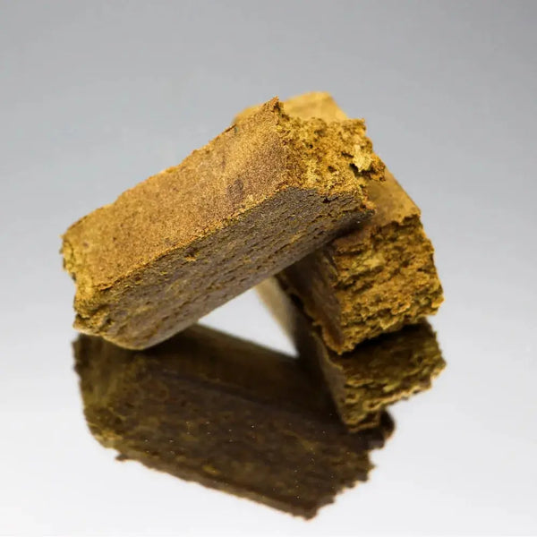 Gros plan sur la résine de CBD Dry Hash Bio de Gr33nz, un extrait naturel issu du pollen de fleurs de CBD, tamisé et pressé à froid, garantissant une concentration optimale en cannabinoïdes.